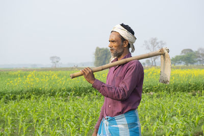 Farmer standing in field holding spade on shoulder