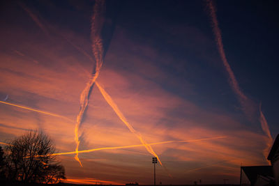 Low angle view of vapor trails in sky at sunset