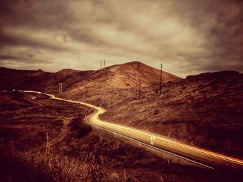 Country road leading towards mountains against cloudy sky