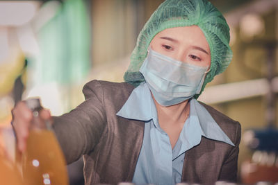 Close-up of woman wearing mask inspecting drink in factory