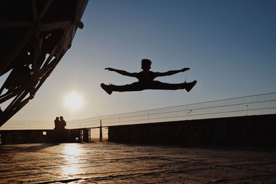 Silhouette man jumping at promenade against sky during sunset