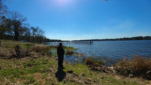 Man standing on riverbank against clear blue sky