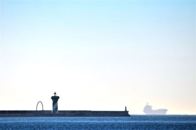 Silhouette man standing by statue on sea against clear sky