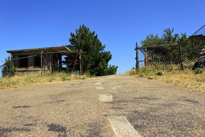 Road by abandoned building against clear blue sky