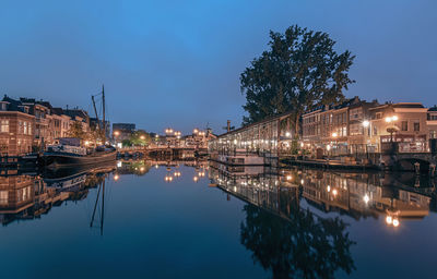 Illuminated buildings by river against sky at night