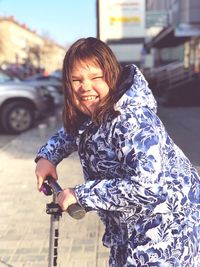Portrait of smiling girl riding push scooter on sidewalk in city