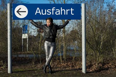 Full length of fashionable young woman standing by road sign on land