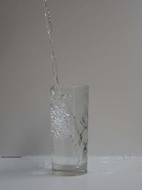 Close-up of glass pouring water against white background