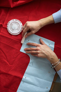 Craftsman woman hands chalked a paper pattern on cotton fabric, top view and close-up