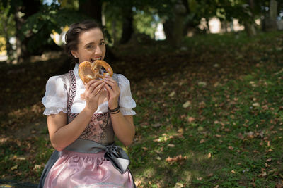 Portrait of woman eating pretzel while sitting on field