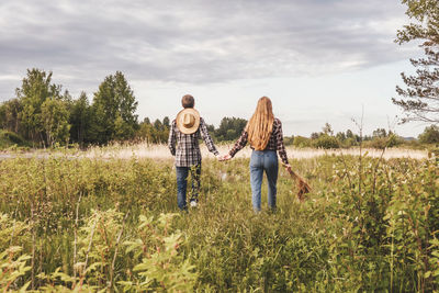 Rear view of friends walking on field against sky