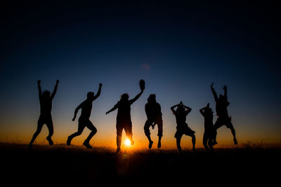 Silhouette people jumping on field against sky during sunset