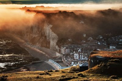 High angle view of buildings in town by mountain during foggy sunset 