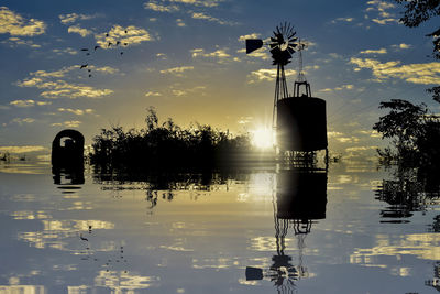 Silhouette built structure by lake against sky at sunset