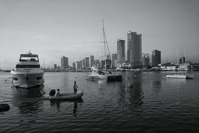 Boats in river by buildings in city against sky