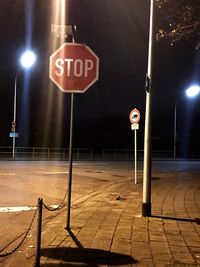 Illuminated road sign against sky at night