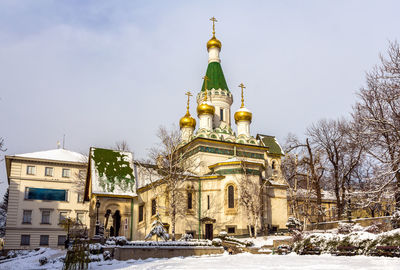Church by building against sky during winter