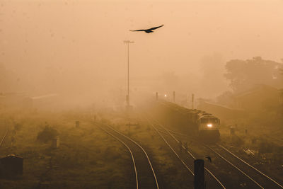 Airplane flying over railroad tracks against sky during sunset