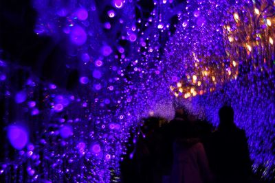 Silhouette people on illuminated purple at night