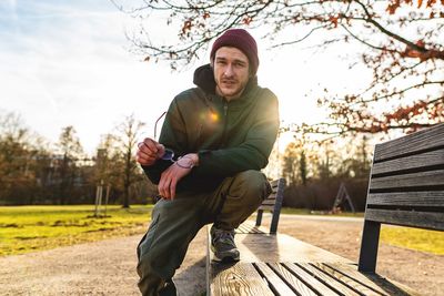 Portrait of young man on bench in park during sunset