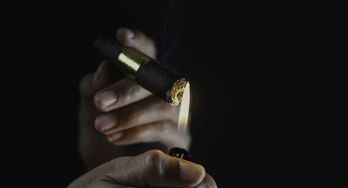 Close-up of hand holding cigarette against black background