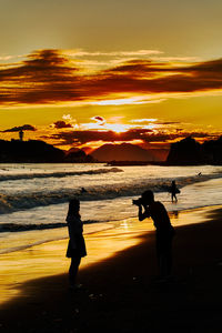 Silhouette people on beach against sky during sunset