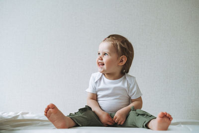 Cuty happy funny baby girl in home clothes sitting on bed at home