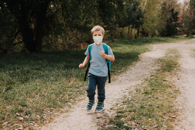 Full length portrait of boy standing on grass against trees