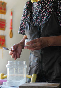 Midsection of woman holding salt bottle while standing by table in kitchen 