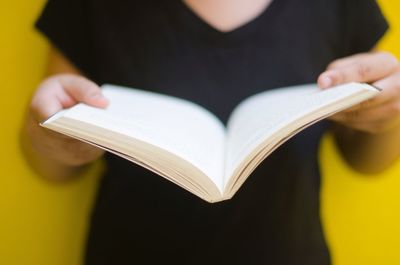Midsection of woman holding book against yellow background