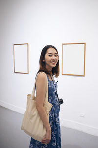 Portrait of a smiling young woman standing against wall