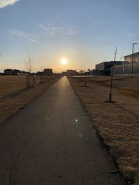 Road amidst buildings against sky during sunset