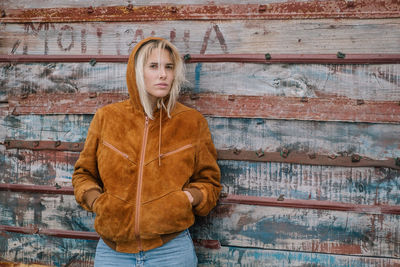 Portrait of young woman standing against wooden wall