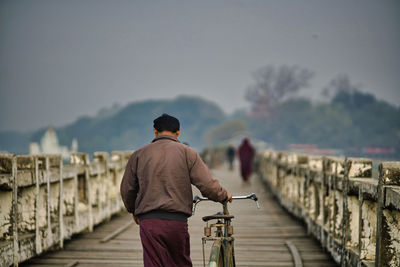 Rear view of man walking with bicycle on footpath