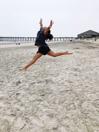 Full length side view of girl with legs apart jumping at beach