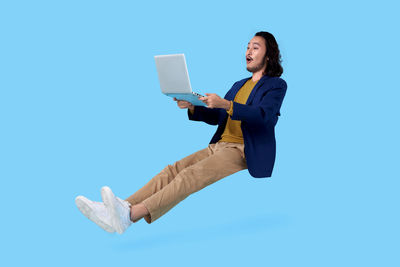 Low angle view of young woman using smart phone against blue background