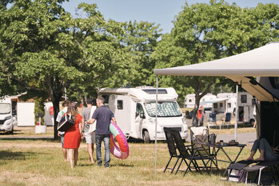 Rear view of family with inflatable rings walking by camper vans at trailer park