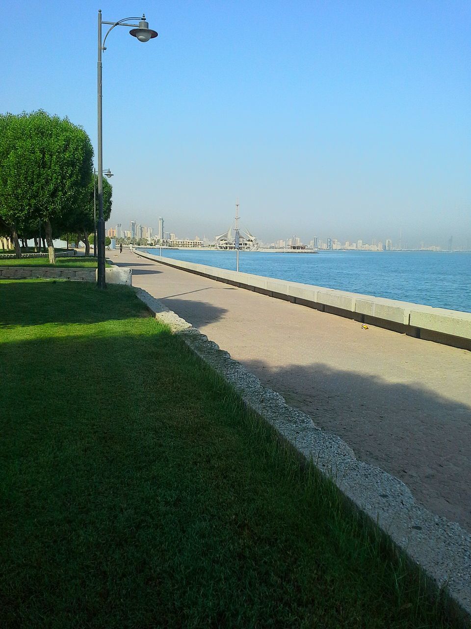 clear sky, water, sea, blue, beach, copy space, tranquility, tranquil scene, sand, street light, shore, nature, horizon over water, scenics, grass, sky, beauty in nature, incidental people, sunlight, outdoors