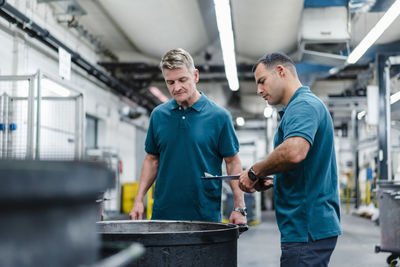 Male professionals looking into barrel while standing in factory