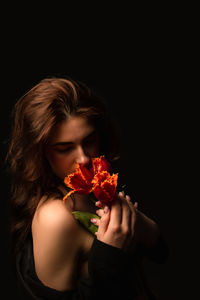 Close-up of woman holding rose against black background