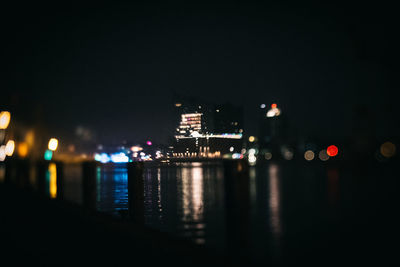 Illuminated cityscape by sea against sky at night