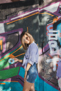 Portrait of young woman standing against graffiti