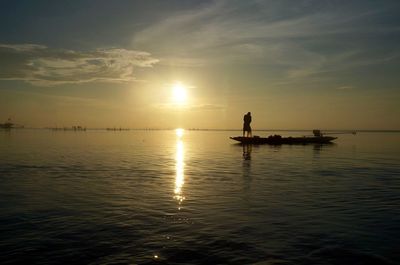 Silhouette man in sea against sky during sunset