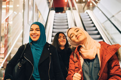 Portrait of happy female friends on escalator in shopping mall