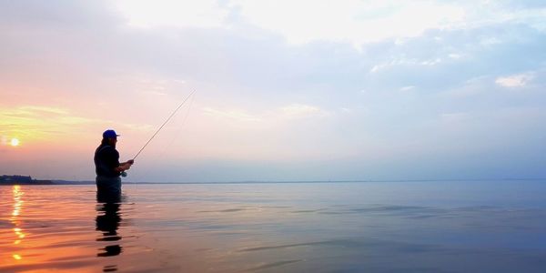 Silhouette mature man fishing in sea against sky during sunset