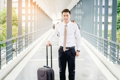 Portrait of businessman with luggage standing on footbridge