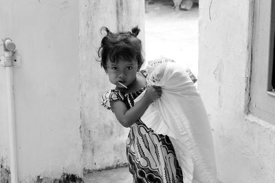 Portrait of girl having lollipop and carrying pillow against built structure