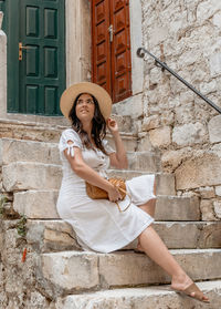 Lifestyle photo of beautiful young woman wearing white dress, sitting on stone stairs