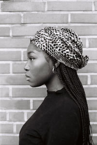 Close-up of woman wearing headwear against brick wall