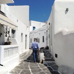 Rear view of man walking on alley amidst white houses at mykonos